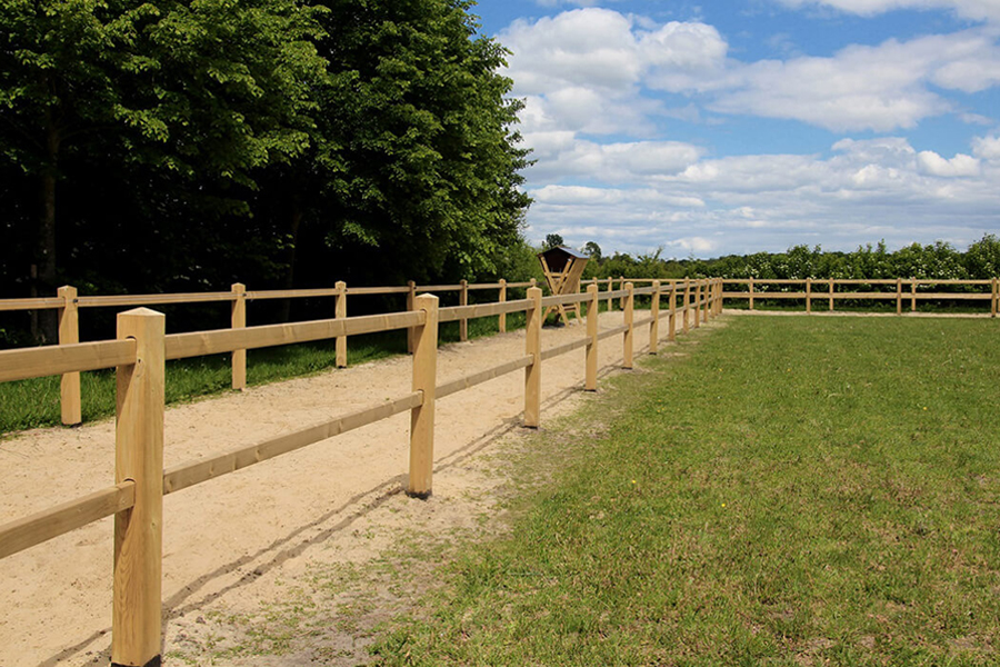 Post and rail fence around a sand track, next to grass paddock